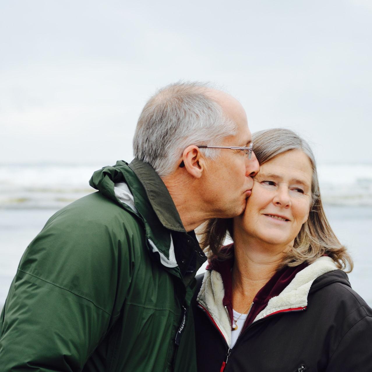 man kissing woman on check beside body of water